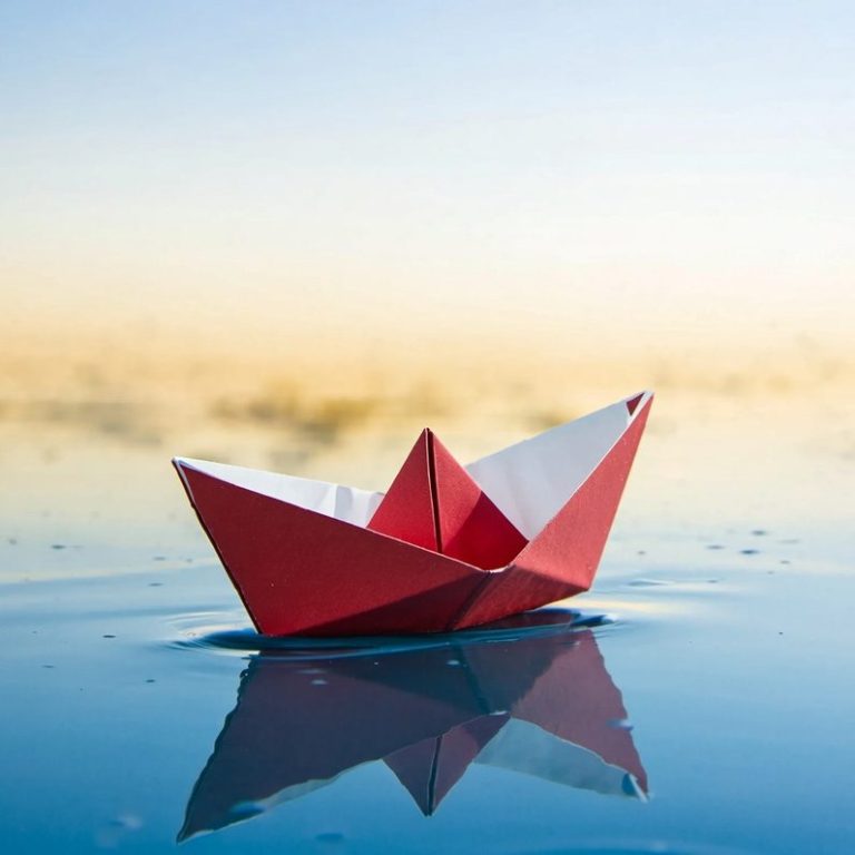 Angelika Stux - Klarheit für den eigenen Weg gewinnen Ein rotes Origami-Schiff schwimmt auf glattem Wasser im Morgenlicht.